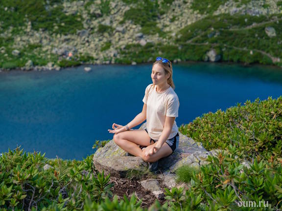 Девушка медитирует на скалистом берегу живописного синего горного озера