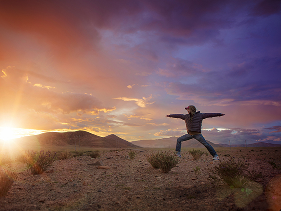 мужчина в позе воина на фоне заката