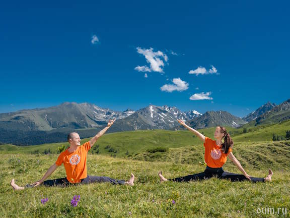 Пара в оранжевом выполняет поперечный шпагат на фоне горного хребта