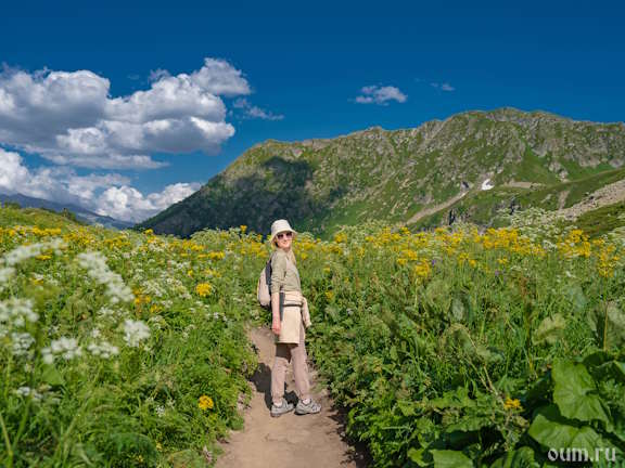 Девушка-турист с рюкзаком стоит на тропе среди лугов в горах