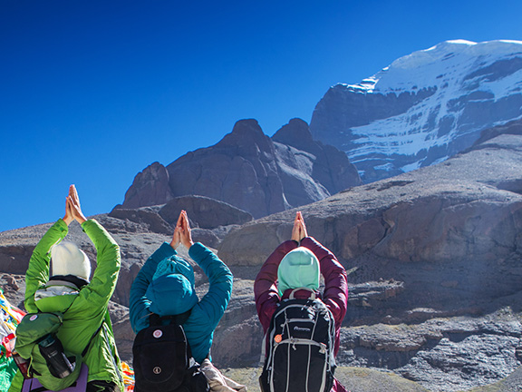 три йогини в намасте на фоне кайлаша