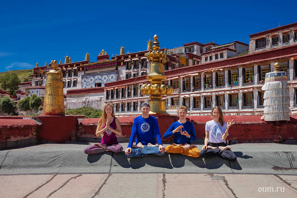 Группа людей в позе лотоса на фоне буддийского монастырского комплекса с золотыми ступами