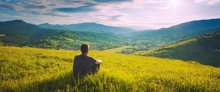 мужчина сидит в траве около гор