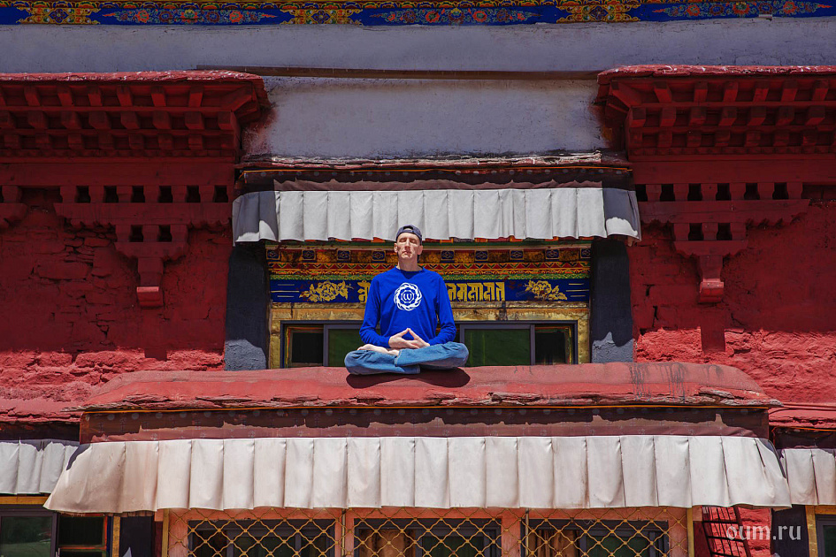 Мужчина в позе лотоса медитирует на карнизе здания, Тибет. Монастырь Ганден