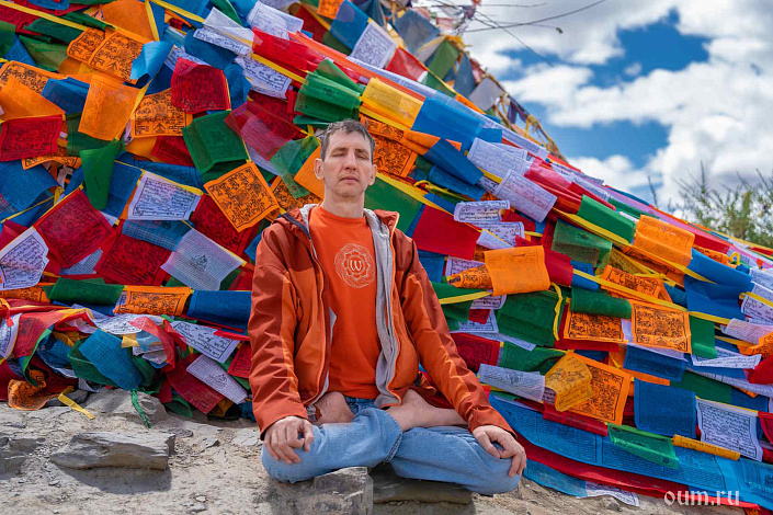 Мужчина в медитации, за спиной буддийские флажки